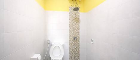 A small, narrow bathroom with white and yellow walls, a toilet, and a shower area.