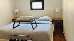 Una camera da letto piccola e luminosa, con un letto, due comodini con lampade, una finestra e un appendiabiti.
