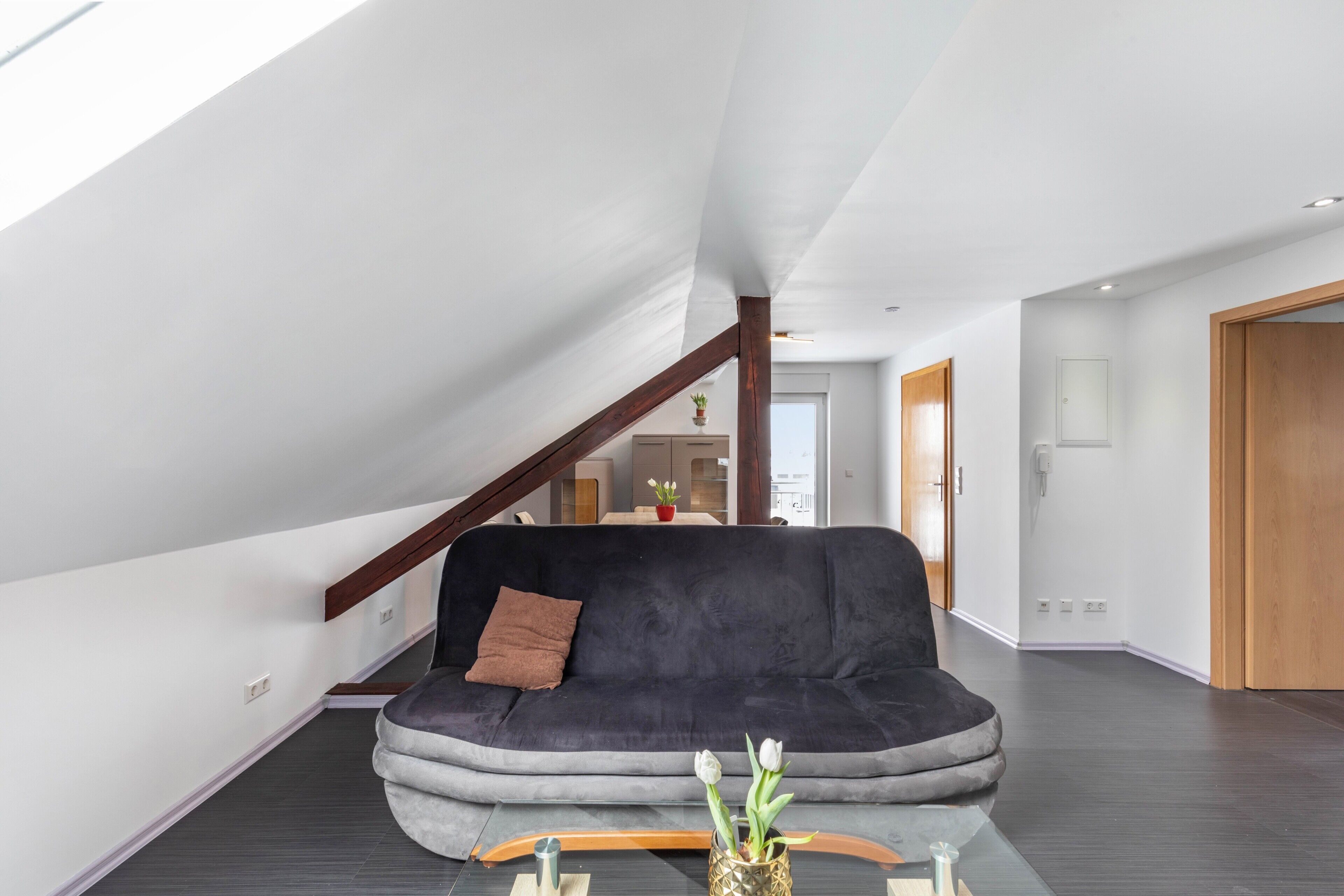 Uma sala de estar moderna com um sofá cinza escuro, uma mesa de centro de madeira e um vaso com flores.