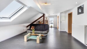 A modern living room with a skylight, a dark sofa, a glass coffee table, and a wooden floor. - Holiday Apartment for Workers Near the Train Station (Babenhausen)
