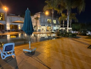 Zona de piscina con una silla de descanso y sombrilla, un edificio con el letrero 'FACILE' y palmeras.