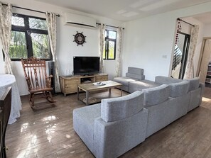 Una sala de estar con sofá gris, una silla de madera, televisor y una mesita.