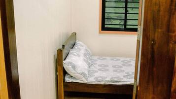Una habitación pequeña con cama individual, cabecera de madera, colchón estampado y ventana con persianas horizontales.