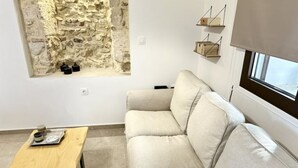 A modern living room with a stone wall, a beige sofa, a wooden table, and a window with blinds. - Nomas Home Kalyves • Beachfront Sea Views, Modern Comfort Steps from the Center (Chania)