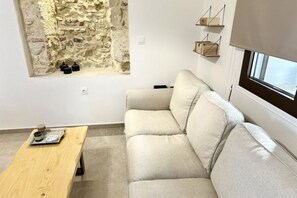 Una sala de estar moderna con una pared de piedra, un sofá color beige, una mesa de madera y una ventana con persianas.