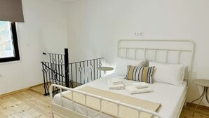 A single-bed room with a white metal frame, a small round table, and a window with a view. - Nomas Home Kalyves • Beachfront Sea Views, Modern Comfort Steps from the Center (Chania)