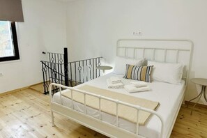 Habitación con una cama individual de estructura metálica blanca, una pequeña mesa redonda y una ventana con vistas.