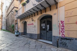 Eine schmale Straße mit einem Gebäude, das einen Balkon, eine mit 'POSTA' beschriftete Tür und Graffiti an den Wänden hat.