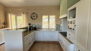 A spacious kitchen with white cabinetry, a large island, and a clock on the wall. - Villa with pool & large shaded terrace - Provence, absolute calm! (Mollans-sur-Ouvèze)