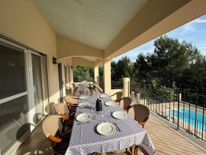 Ein überdachter Essbereich im Freien mit Blick auf einen Pool, ausgestattet mit Stühlen und einem für das Essen gedeckten Tisch.