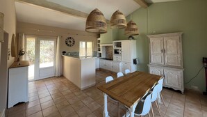 A kitchen with a wooden table, white chairs, a clock, and hanging wicker lights. - Villa with pool & large shaded terrace - Provence, absolute calm! (Mollans-sur-Ouvèze)