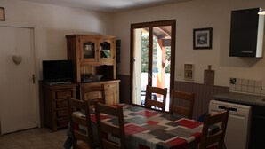 A compact kitchen with wooden cabinets, a dining table with chairs, a television, and a refrigerator. - Quiet gite near Sarlat (Tamniès)