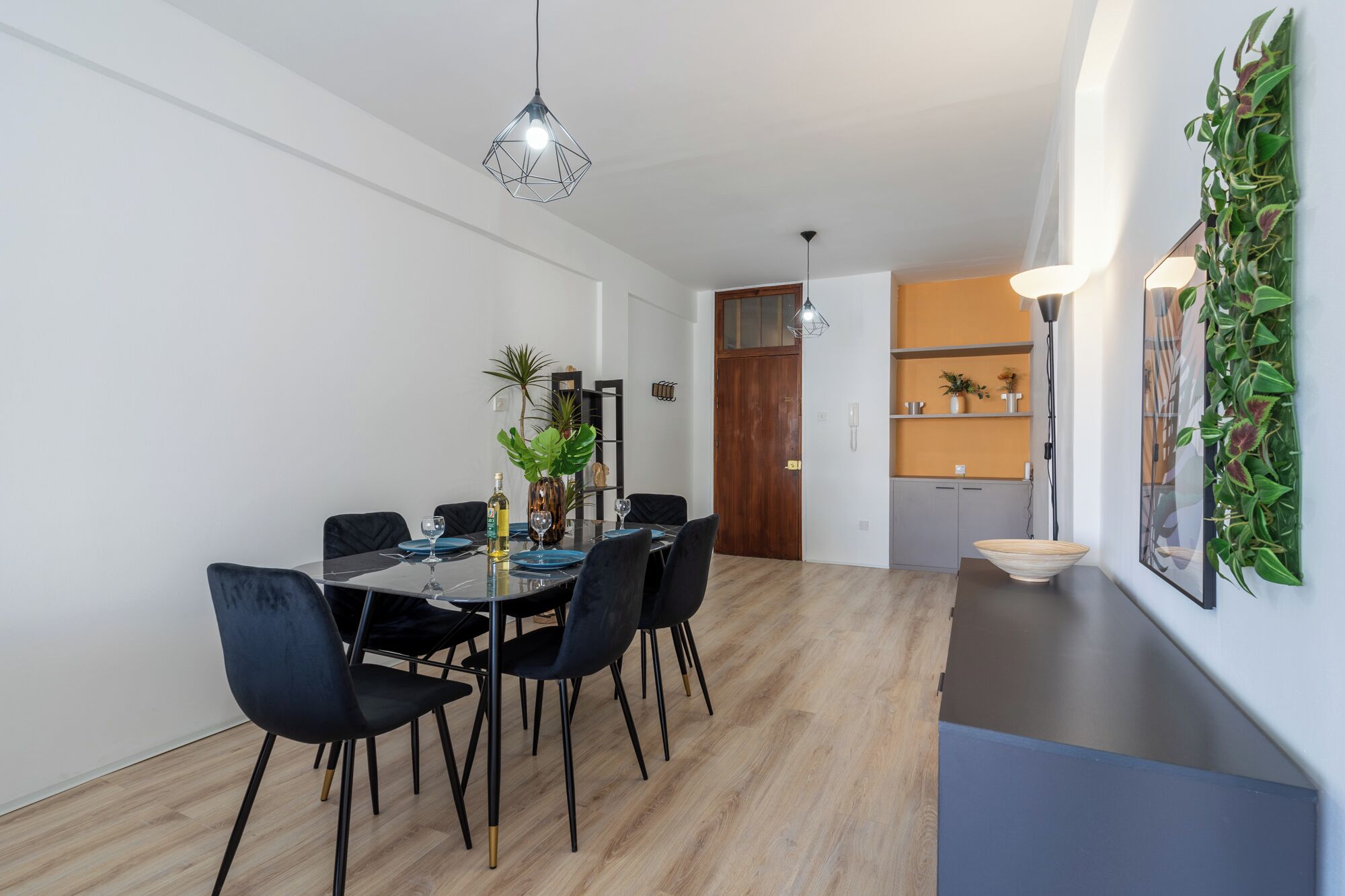 Een moderne eetruimte met een glazen tafel, zwarte stoelen en hanglampen.