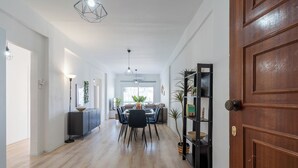 A spacious hallway with a wooden floor, a dining area with a table and chairs, and a bookshelf with plants. - Citrus 3-BR Apt. & Balcony in Larnaca (Larnaca)