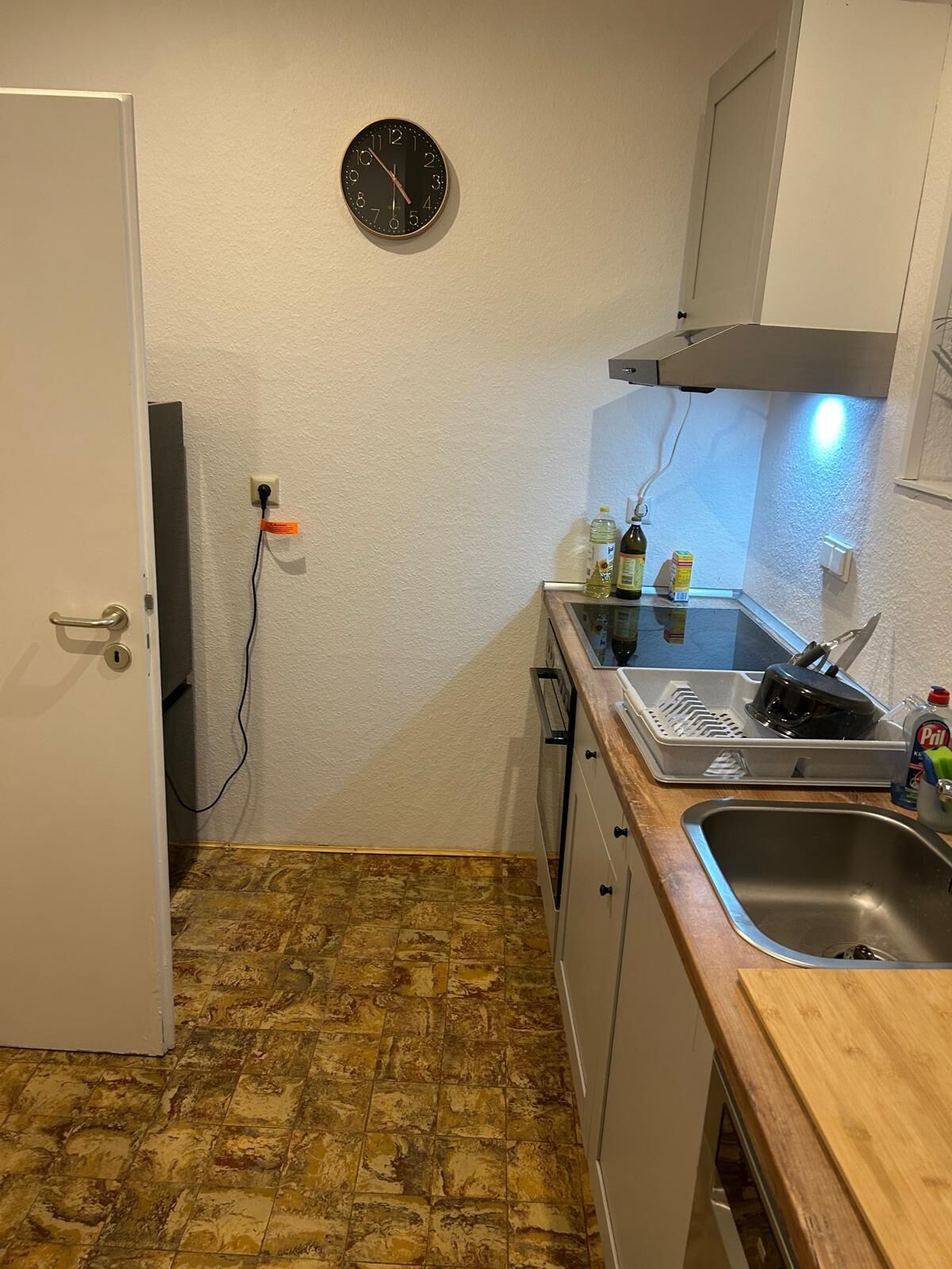 A compact kitchen with a clock on the wall, a sink, and a stove.