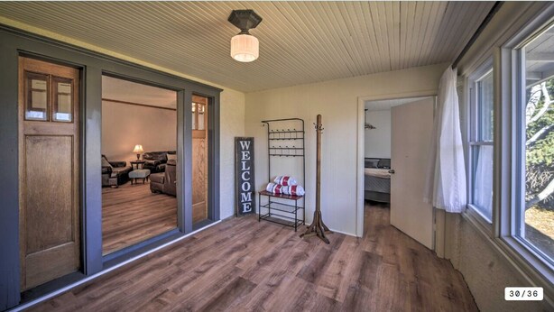 Um corredor amplo com piso de madeira, um letreiro com a palavra 'WELCOME', um porta-roupas e uma cama ao fundo.