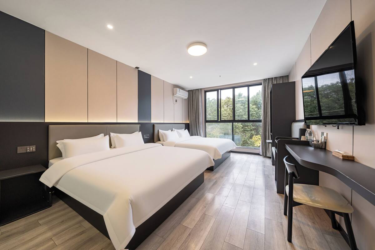 A modern hotel room with two beds, a desk, and a TV.