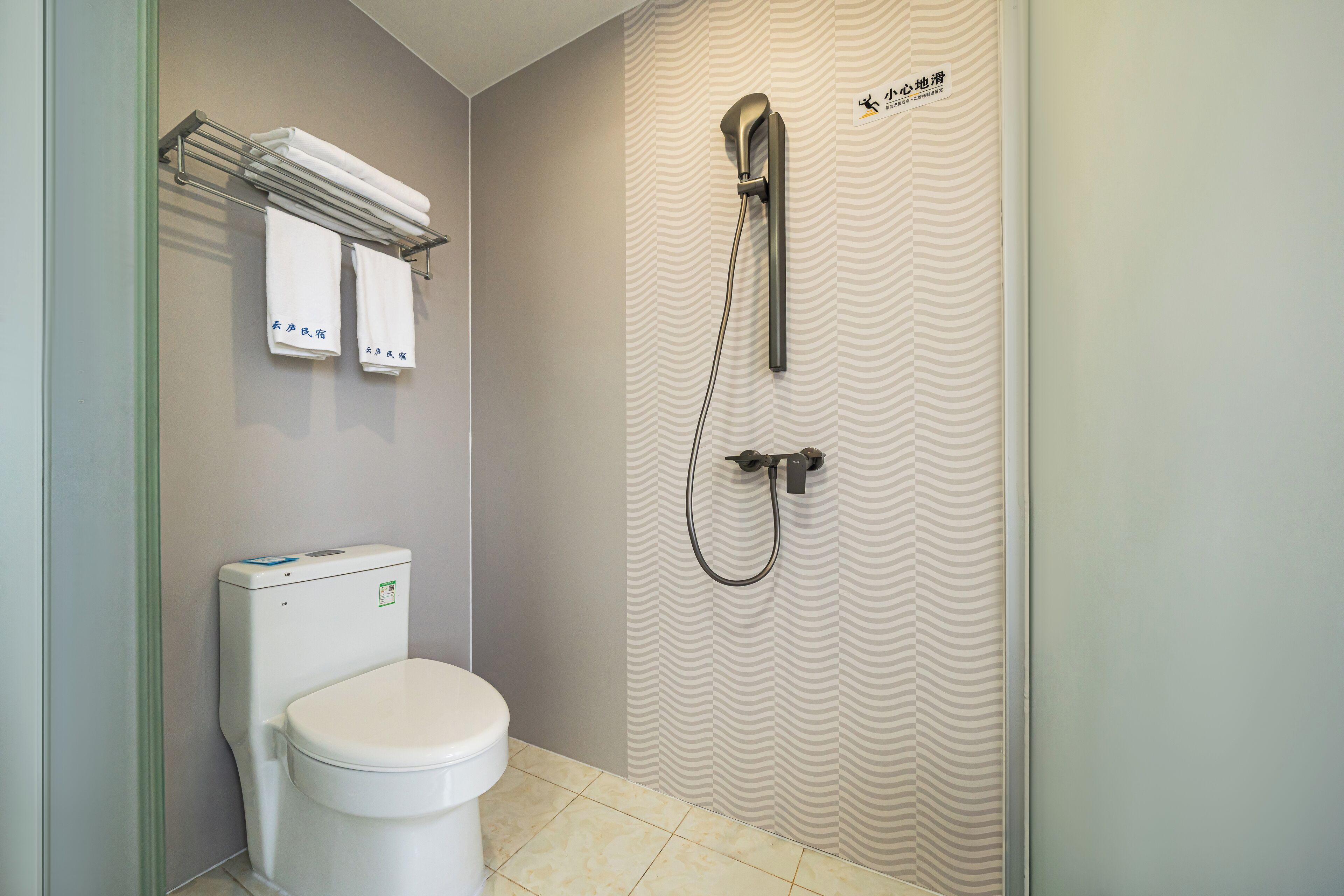 A bathroom with a toilet, a shower, and a towel rack with towels.