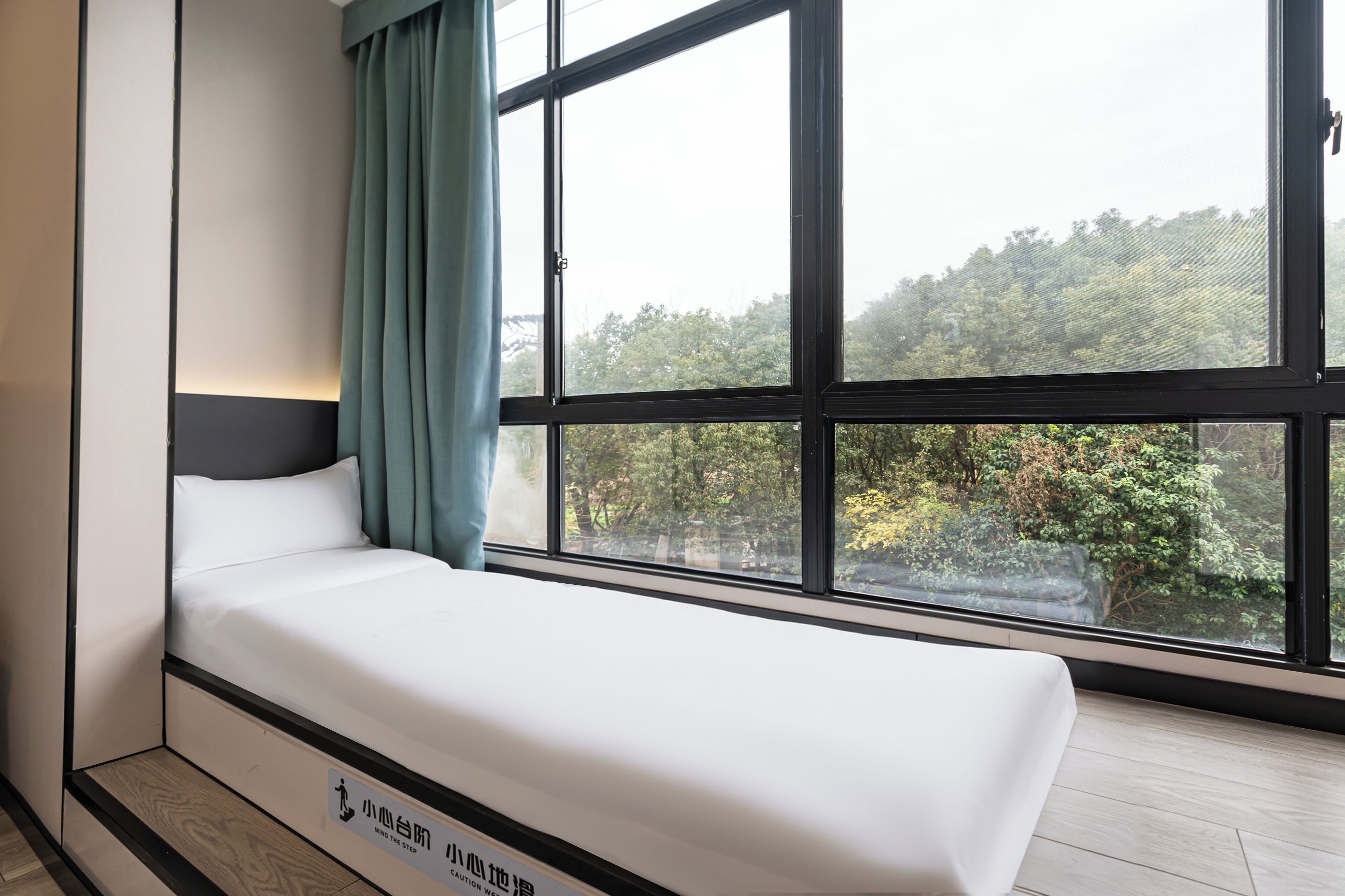Quarto moderno com cama, janelas amplas e vista para árvores.
