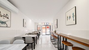Egy modern étkező, hosszú asztalokkal és bárszékekkel, a falakon elhelyezett műalkotásokkal, és letisztult, minimalista dizájnnal.