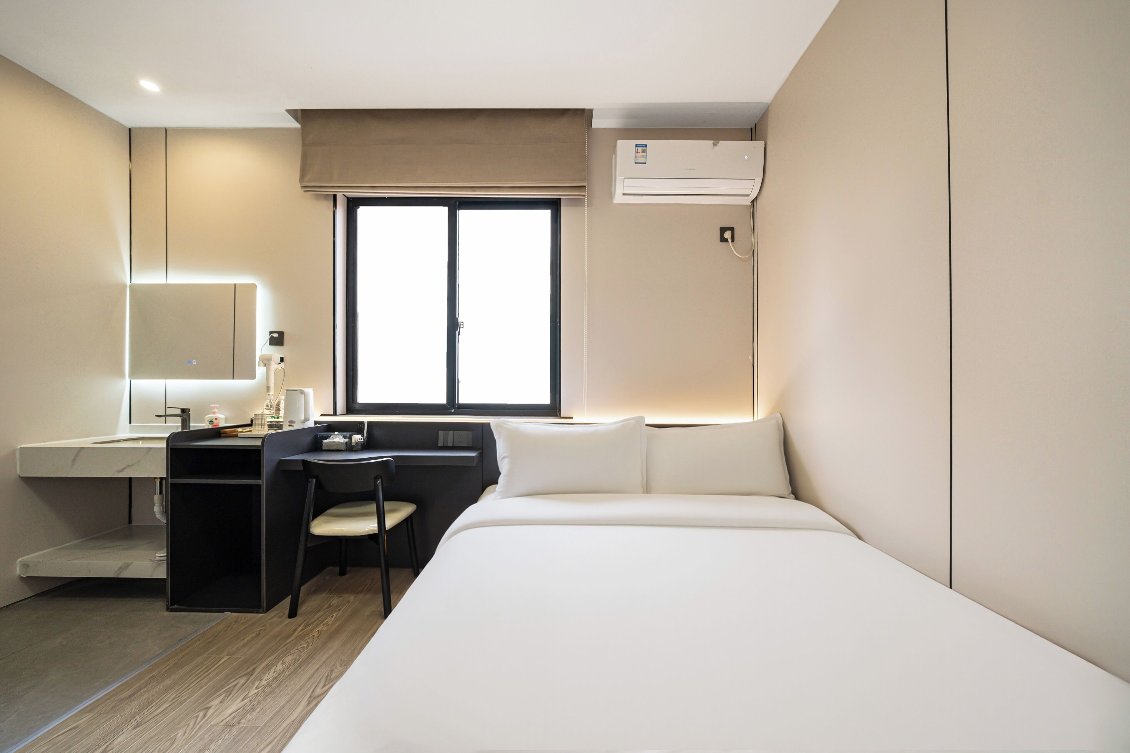 Una habitación de hotel moderna con cama, escritorio, silla y un ventanal grande.