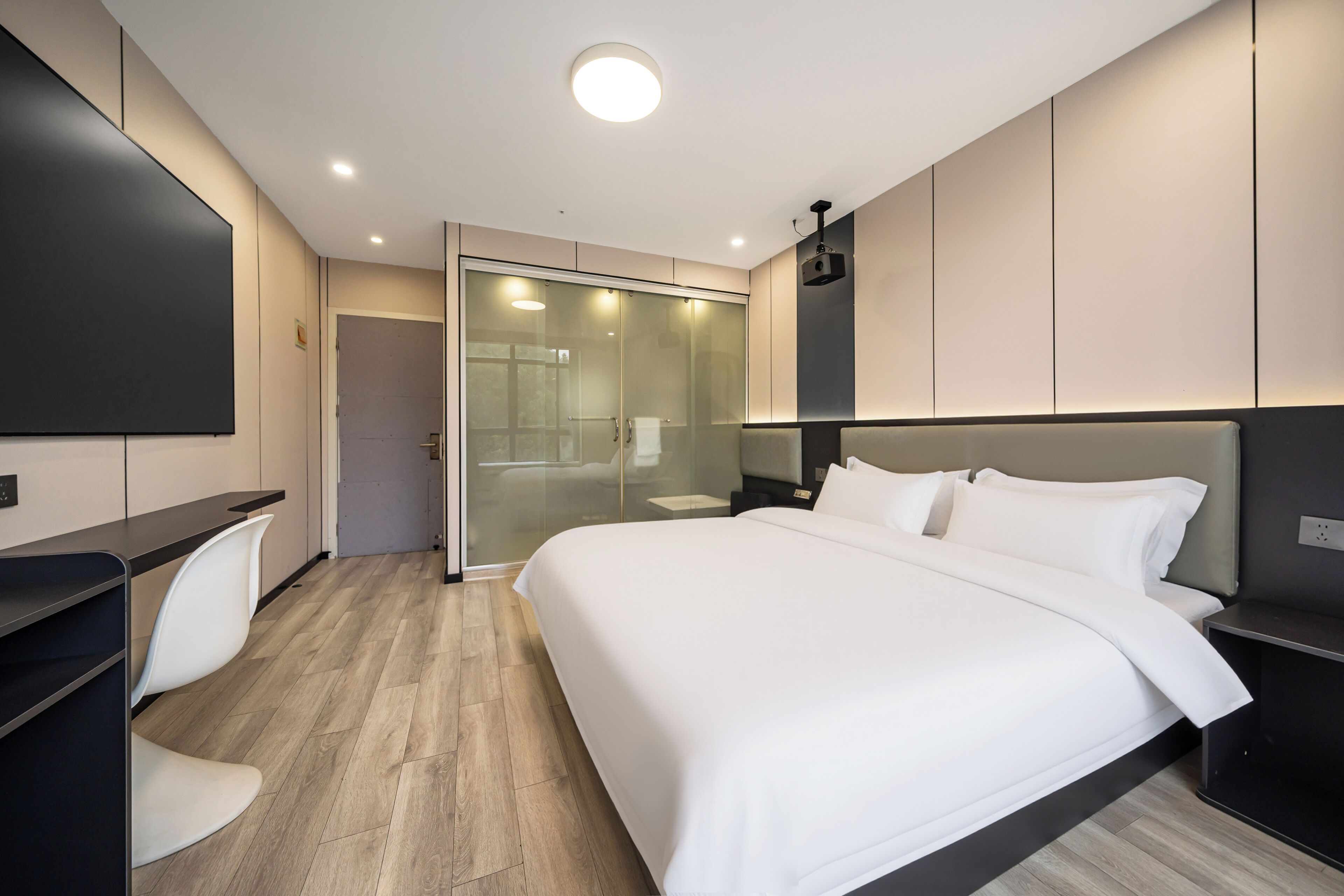 Een moderne hotelkamer met een groot bed, een bureau en een douchecabine van glas.