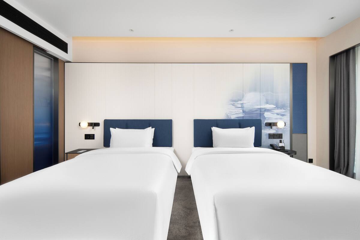 Habitación de hotel con dos camas, un ventanal con vistas a un paisaje nevado y un diseño moderno con colores neutros.