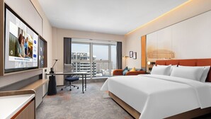 Una moderna camera d'albergo con un letto grande, una scrivania con sedia, una TV a schermo piatto e vista sulla città attraverso ampie finestre.