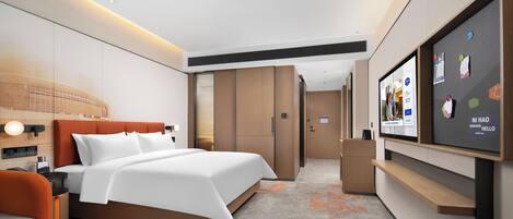 Una habitación de hotel moderna con una cama grande, un televisor montado en la pared y un área de descanso con un sofá y un sillón.