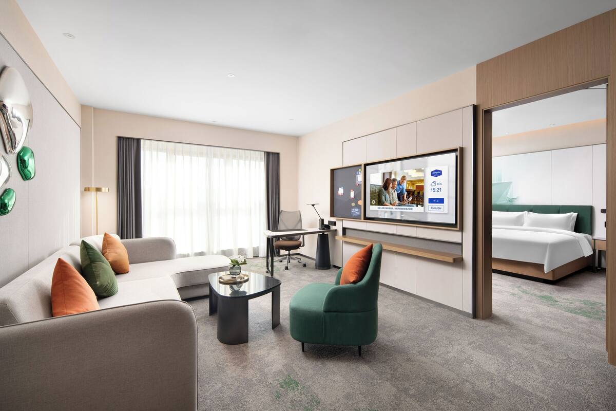 Una habitación de hotel moderna con sofá, sillón, televisor, escritorio y cama.