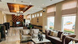 A hotel lobby with a reception desk, seating area with sofas and chairs, a chandelier, and large windows. - The Vineyard at Merlot TwinLakesTagaytay (Laurel)