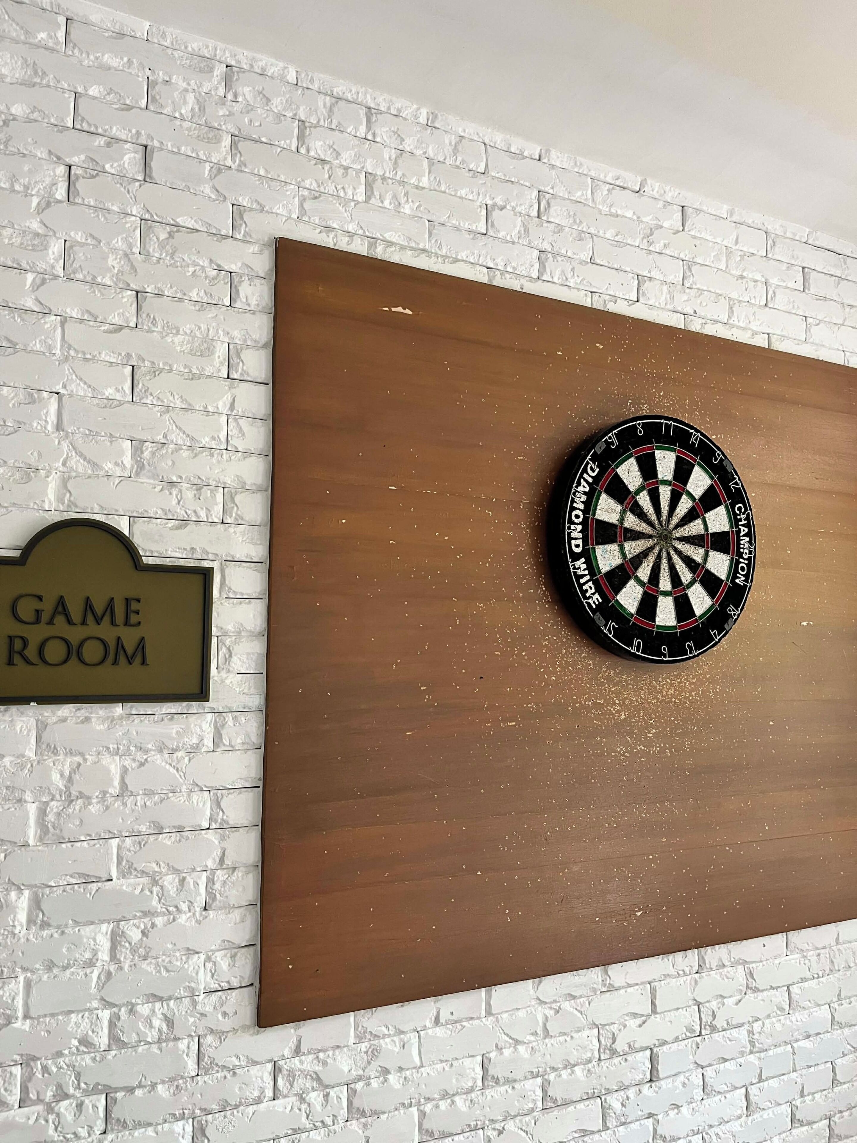 Eine Dartscheibe an einer Ziegelwand, mit einem Schild, auf dem 'GAME ROOM' steht.
