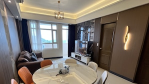 A modern living room with a round dining table, comfortable seating, a flat-screen TV, and a large window offering a view. - The Vineyard at Merlot TwinLakesTagaytay (Laurel)