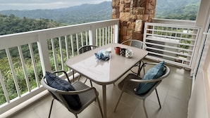 A balcony with a table and chairs, a stone pillar, and a view of a hilly landscape. - The Vineyard at Merlot TwinLakesTagaytay (Laurel)