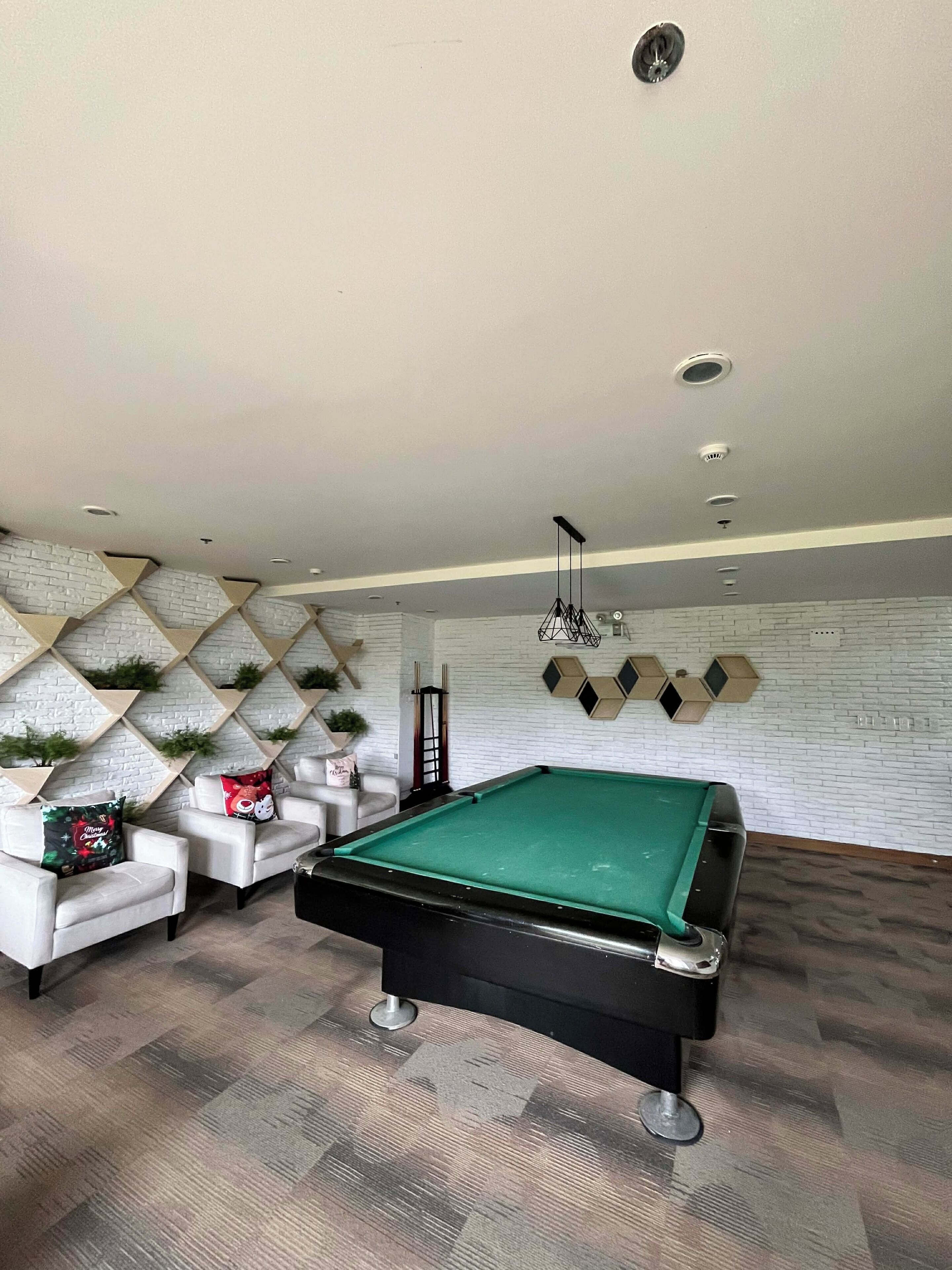 A pool table in a room with a white brick wall, a sofa, and a ceiling light fixture.