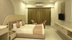 A modern hotel room with a bed, a desk, a chair, a television, and an air conditioning unit. - Hotel Shree Khodal (Sanand)