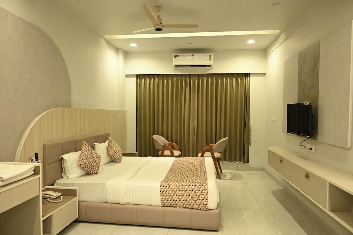 A modern hotel room with a bed, a desk, a chair, a television, and an air conditioning unit.