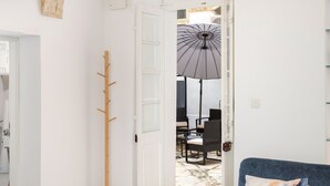 A living room with a blue sofa, a patterned rug, a coat rack, and a view of an outdoor dining area through an open door. - Traditional APT with Internal Courtyard (Valletta)