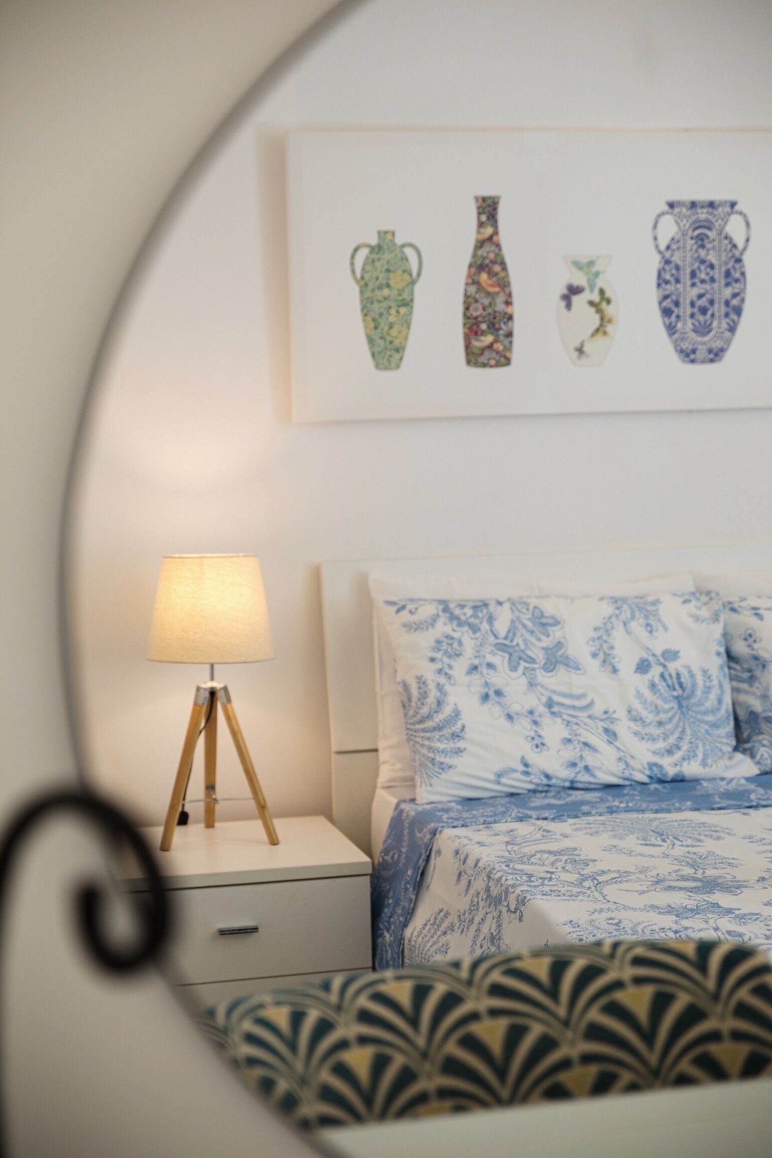 A bedroom with a bed, a bedside lamp, a nightstand, and a wall-mounted picture of vases.