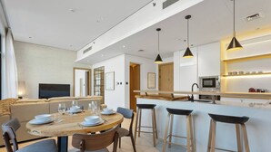 A modern kitchen with a central island, bar stools, and a dining area with a round table and chairs. - Urban Chic 1 Bedroom w/ big Balcony Kitchen in JVC (Jumeirah Village Circle (JVC))