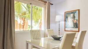 Een eetruimte met een witte tafel en stoelen, een schaal op de tafel, een lamp en een schilderij aan de muur.