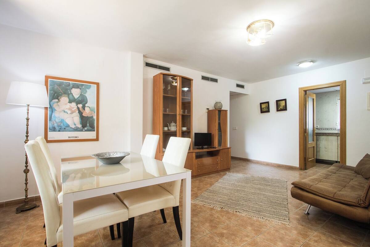Ein Wohnzimmer mit Esstisch, Stühlen, einer Couch, einem Fernseher und einem Schrank.