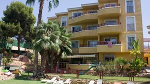 Een meerlaags hotel met balkons, een zwembad en palmbomen.