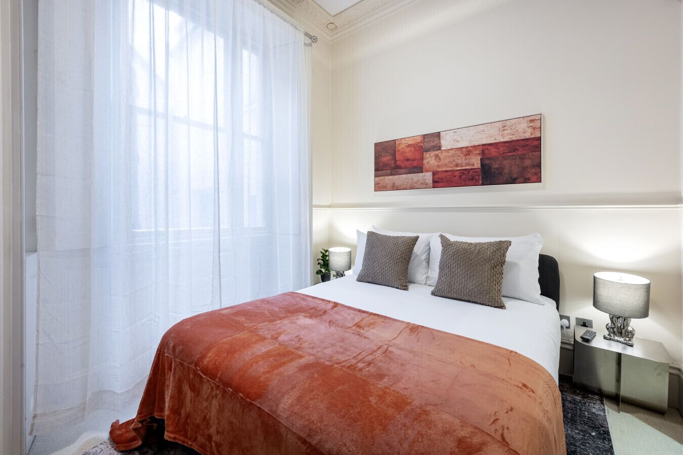 Ein Hotelzimmer mit einem großen Bett, weißer Bettwäsche, einer braunen Tagesdecke, einem Bild an der Wand und einem Nachttisch mit Lampe.