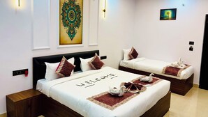 A hotel room with a large bed, two smaller beds, a decorative wall piece, and a ceiling fan. - The Ravishya Retreat (Ayodhya)