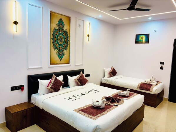 A hotel room with a large bed, two smaller beds, a decorative wall piece, and a ceiling fan. - The Ravishya Retreat (Ayodhya)
