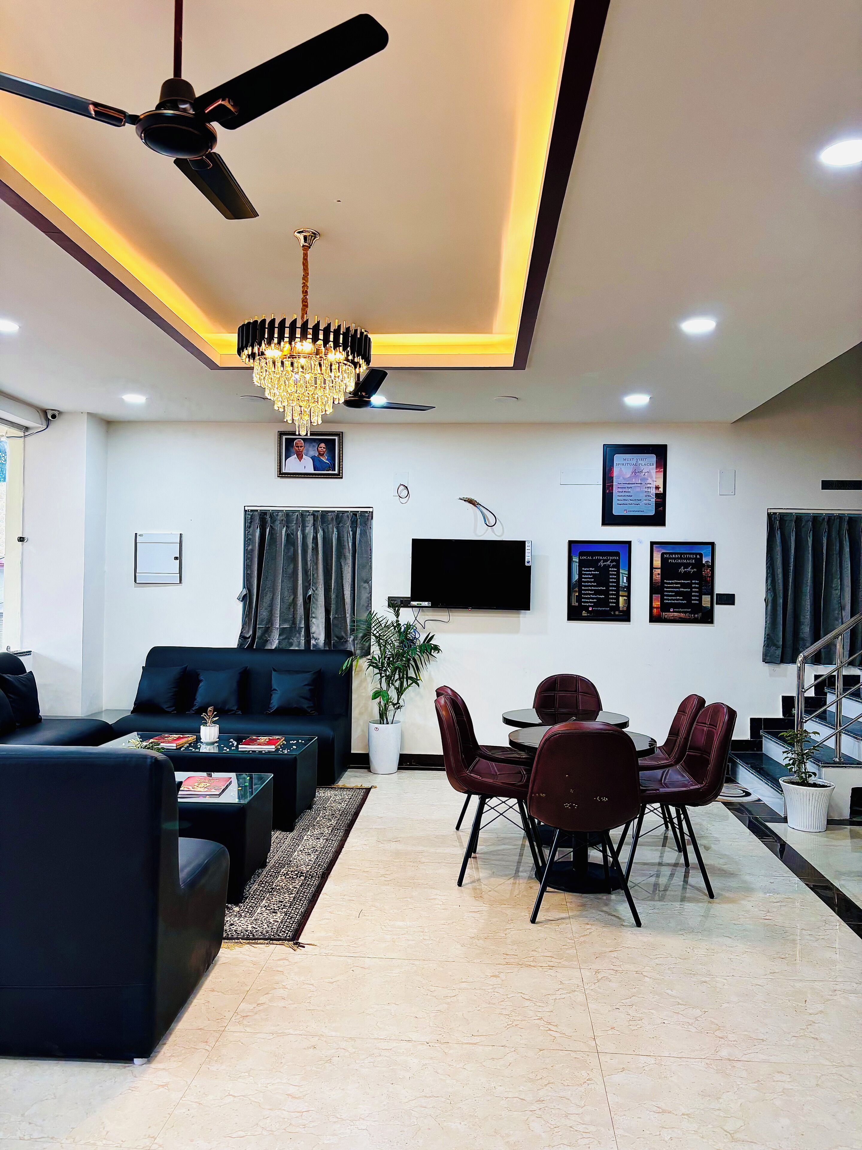 A modern living room with a sofa, coffee table, dining table, chairs, a chandelier, ceiling fan, TV, and a staircase.
