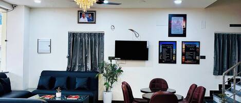 A modern living room with a sofa, coffee table, dining table, chairs, a chandelier, ceiling fan, TV, and a staircase.