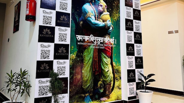 A wall with a large mural of a deity, QR codes, and potted plants. - The Ravishya Retreat (Ayodhya)