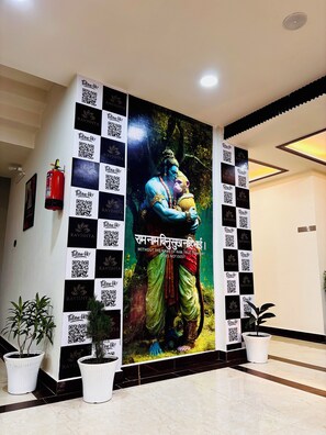 A wall with a large mural of a deity, QR codes, and potted plants. - The Ravishya Retreat (Ayodhya)